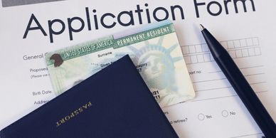 A passport, U.S. permanent resident card, and application form with a pen.