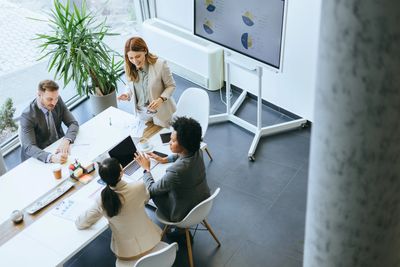 Four professionals engaged in a collaborative business meeting with charts on a screen.