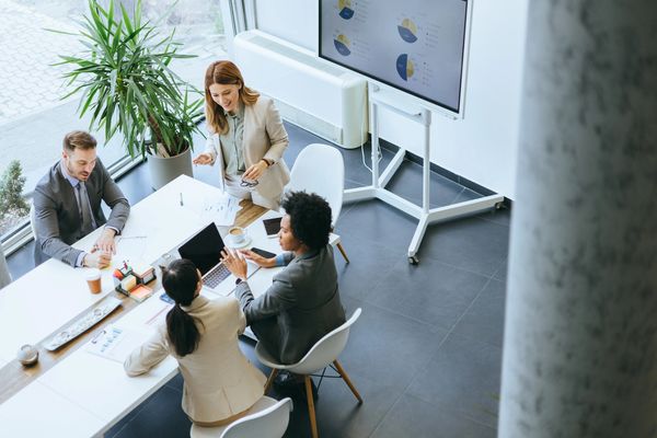 Business team collaborating in a bright office with charts on screen.