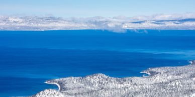 Snow-covered landscape with a deep blue lake and distant mountains.