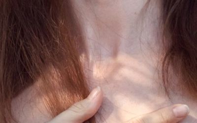 Close-up of a person's neck and hand with soft lighting.