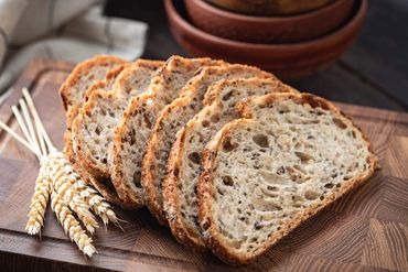 Sliced whole grain bread on a wooden board with wheat stalks.