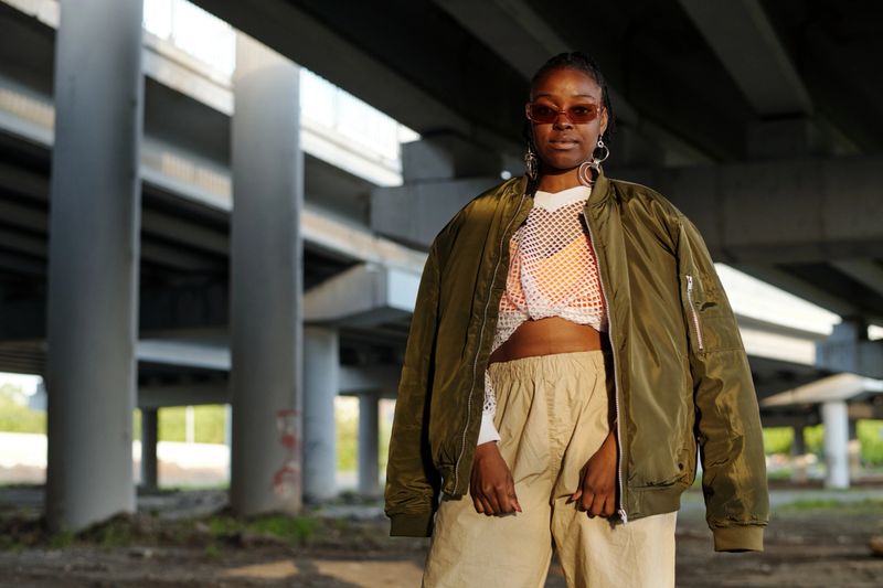African American woman wearing casual outfit standing under a bridge in urban setting showing relaxed and confident demeanor