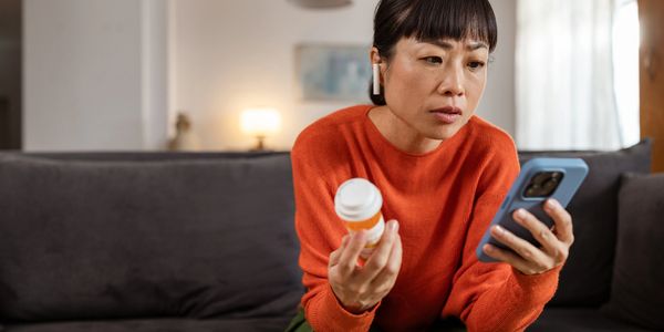 Woman checking prescription details on her phone while holding a medication bottle.