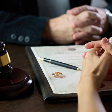 Two people discussing divorce with wedding rings and a gavel on the table.