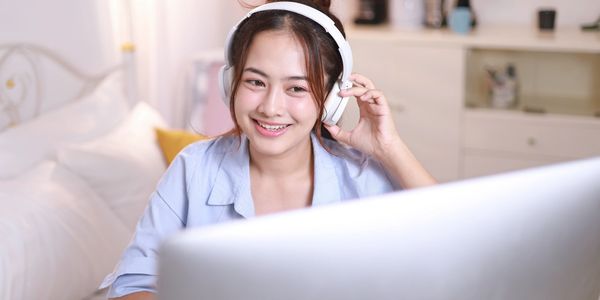 Young woman wearing headphones and smiling at a computer screen.