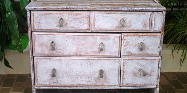 Rustic whitewashed wooden dresser with six drawers and vintage handles.