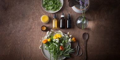A flat lay of fresh flowers, essential oils, and herbal ingredients on a wooden table.