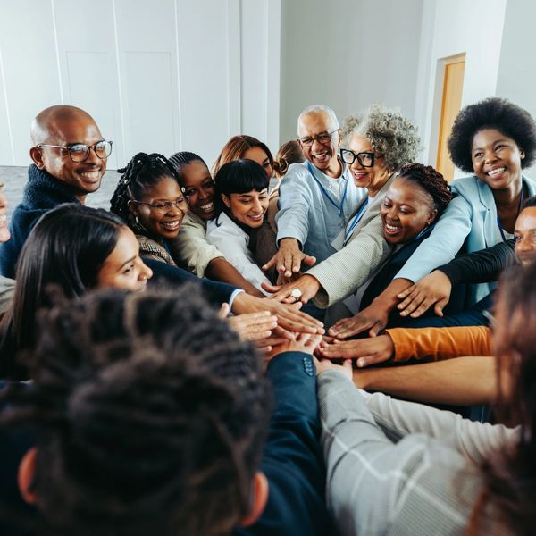 A diverse group of people joining hands in a team huddle indoors.