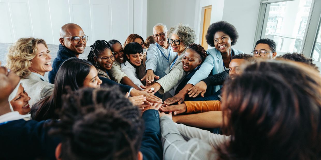 A diverse group of people joining hands in a team huddle indoors.