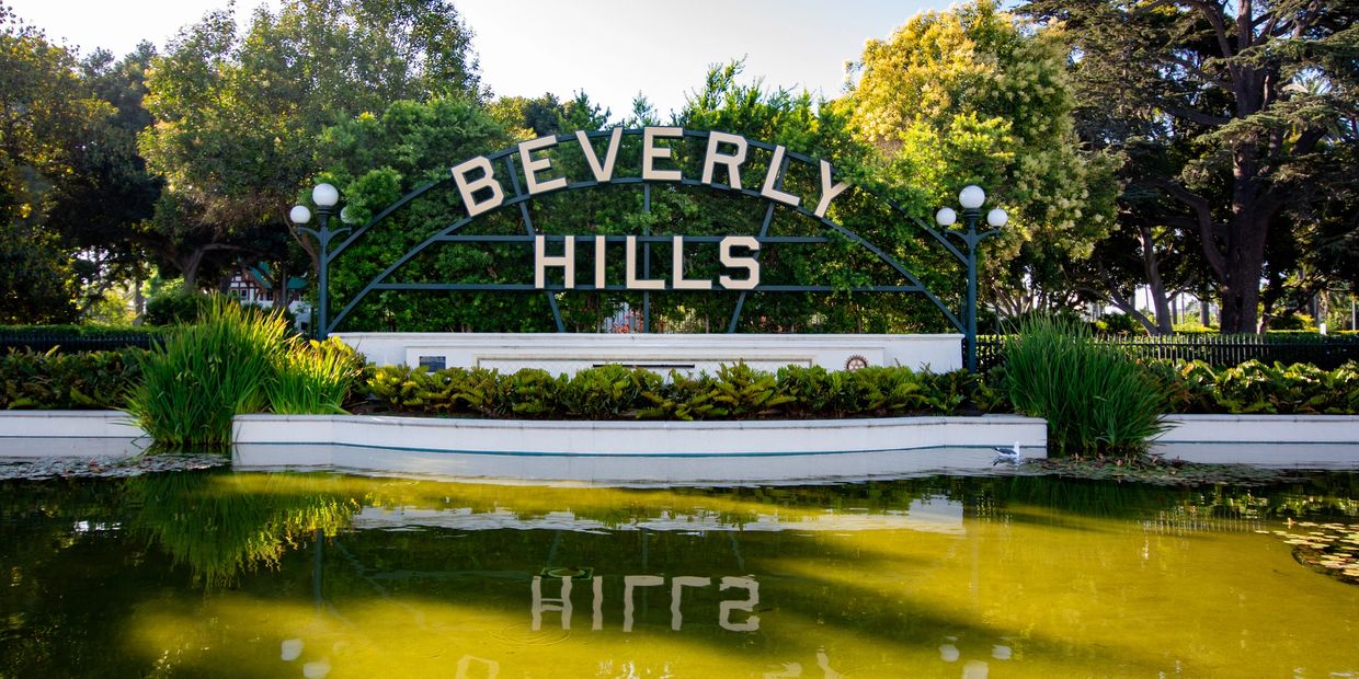 Beverly Hills sign with greenery and water reflection.