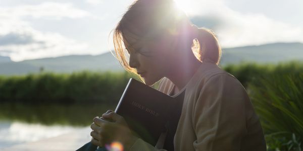Girl reading book sitting by river at sunset