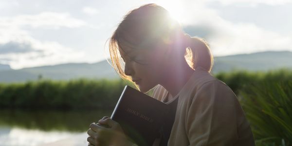 Girl reading book sitting by river at sunset