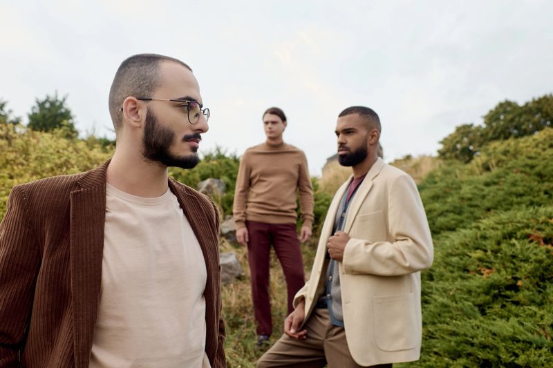 Three handsome men pose confidently in a vibrant autumn field, highlighting seasonal fashion trends.