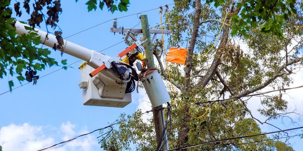 Worker in bucket truck repairing power lines on a sunny day.