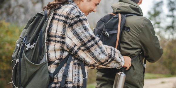 Woman adjusts man's backpack on a hiking trail. Couple hiking in nature.