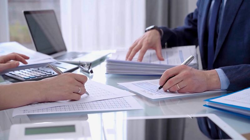 Business colleagues accountants or auditors reviewing financial data in office. Two professionals analyzing paper reports and using calculators. Audit and taxes.