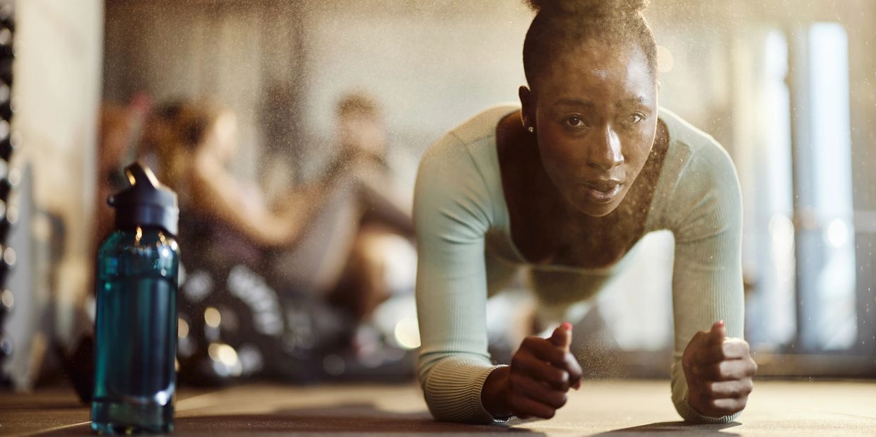 Woman doing a plank exercise in a gym with a water bottle nearby.