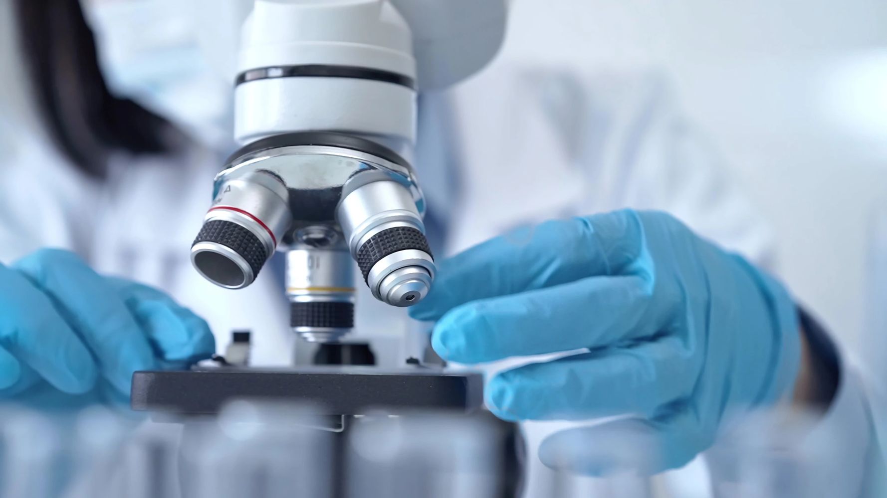 Scientist wearing blue gloves adjusting a microscope in a lab.