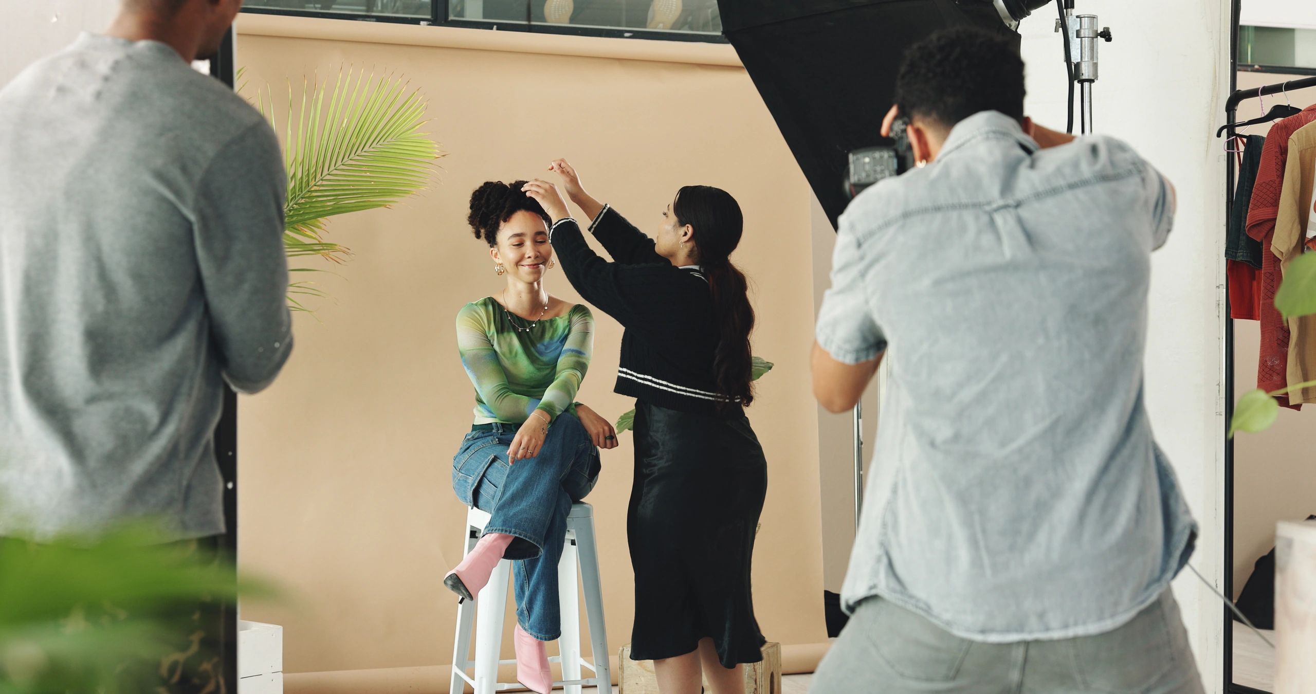 Photographer is focusing camera, make-up artists is working with busty seated model