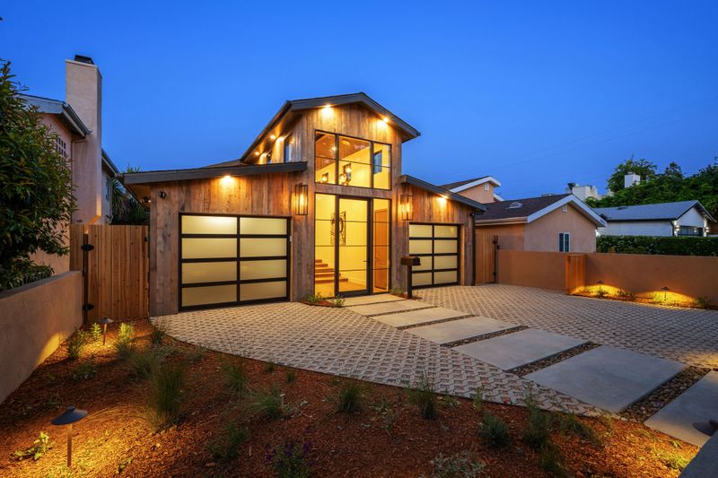 A modern wooden house exterior with an illuminated driveway under the twilight sky. California