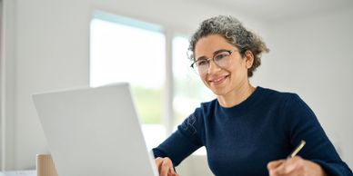 Smiling woman working on a laptop and taking notes at a desk.