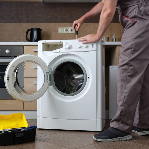 Technician repairing a front-load washing machine in a modern kitchen.
