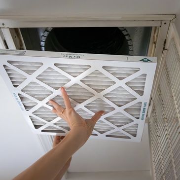 Person installing a new air filter in a ceiling vent.