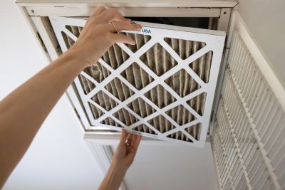 Person replacing an air filter in a vent.