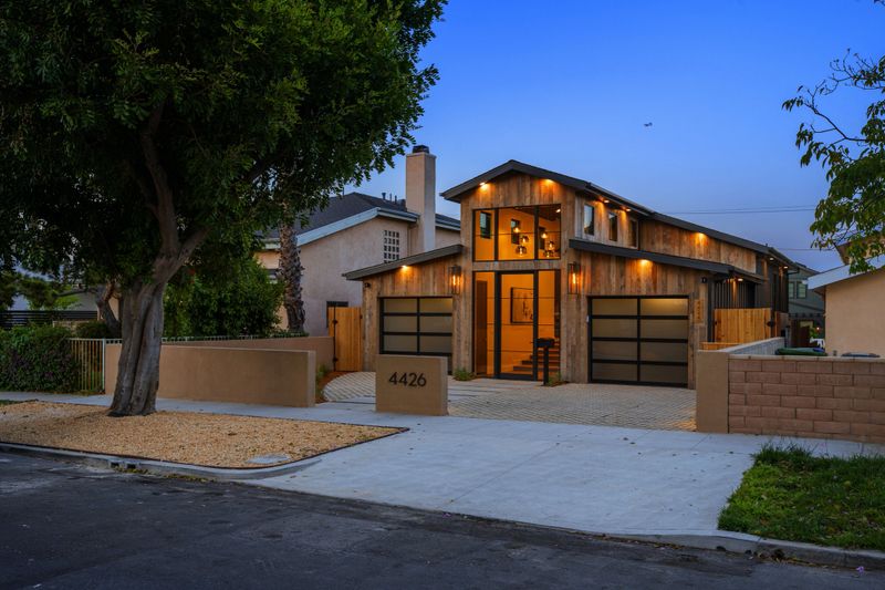 Modern suburban house with elegant lighting at dusk, featuring a tree-lined street and contemporary architecture.
