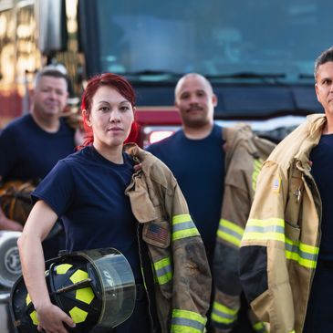 A group of firefighters standing confidently in front of fire trucks.