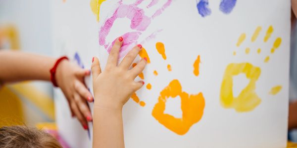 Children pressing colorful handprints on a white wall.