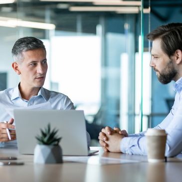 Two men engaged in a serious business discussion at a modern office desk.