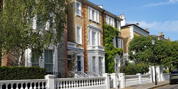 Row of elegant townhouses with white fences and lush greenery on a sunny day.