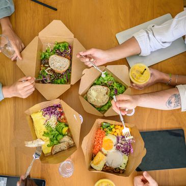Friends sharing a healthy meal with salads and smoothies at a wooden table.
