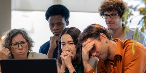 A group of diverse colleagues look stressed while working on a laptop.