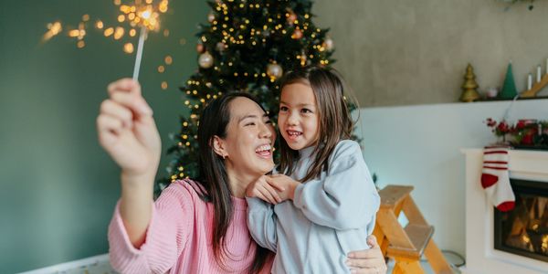 Mother and daughter joyfully celebrate Christmas with a sparkler near a decorated tree.