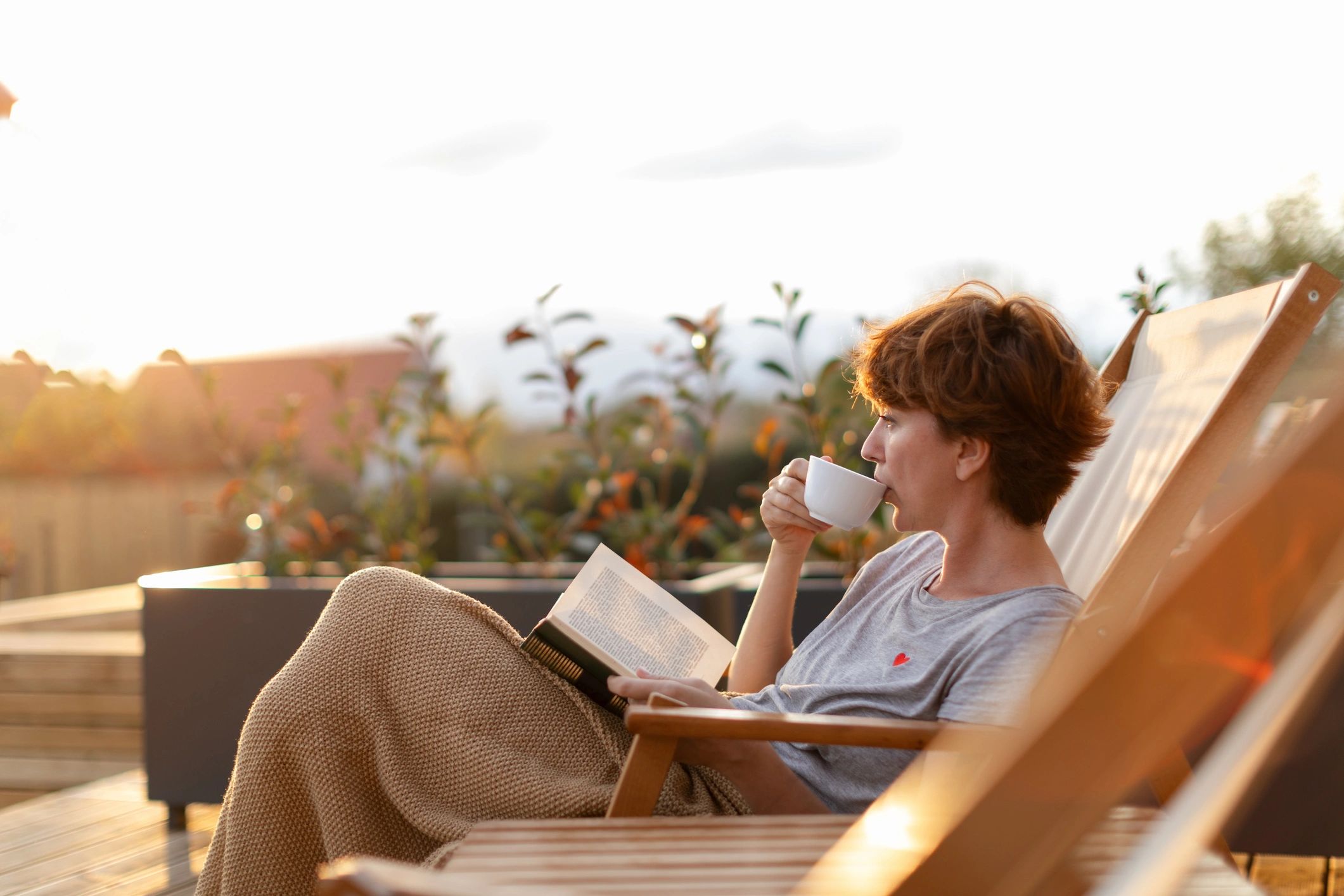 Person reading a book and drinking coffee outside.