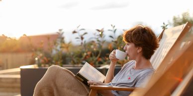 Woman enjoying coffee and reading a book outdoors in the sunlight.