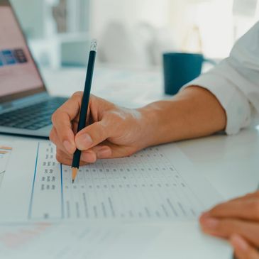 Person analyzing financial data with laptop and charts on desk.