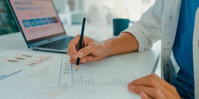 Person analyzing financial data with charts and laptop on a desk.