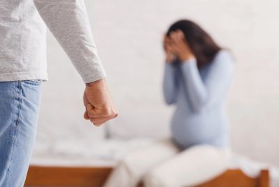 A clenched fist confronts a distressed pregnant woman sitting on a bed.