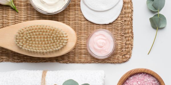 Spa essentials: brush, creams, towel, bath salts, and flowers arranged on a mat.