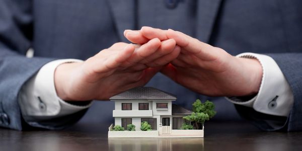 A person protects a miniature house model with their hands.
