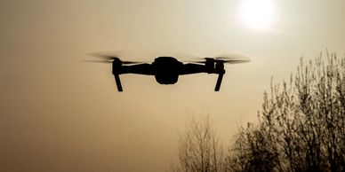 Silhouette of a drone flying against the sunset sky.
