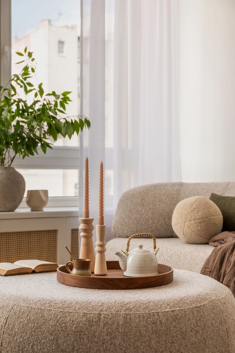 Stylish interior with a wooden cabinet adorned with potted plants, decorative objects, and books. A vibrant art piece featuring a sunburst design adds a pop of color. Cozy seating area visible in the background.