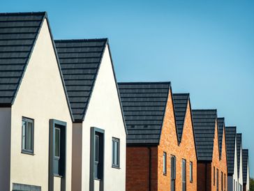 Row of modern houses with black roofs and blue sky.