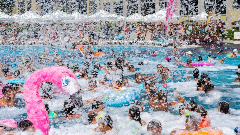 Foam party with inflatable mattresses in form of pink flamingos in pool. People have fun in swimming pool on sunny day in summer. People are unrecognizable. Selected focus. Recreation.