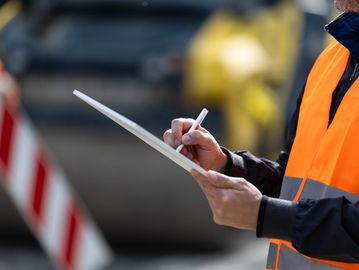 Worker in orange vest writing on a clipboard.