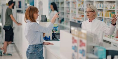 A customer speaks with a pharmacist at the counter in a pharmacy.